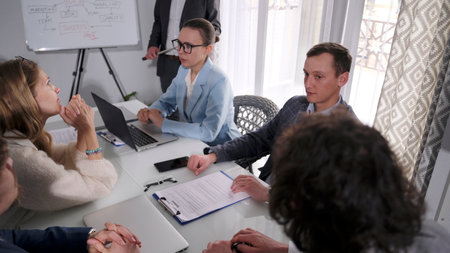 A group of young business people are sitting at a table and working on a project. The atmosphere is...