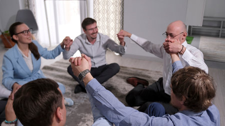 A peaceful scene of meditation and Unity of the company's employees in the family office at the team building. A group of people are sitting on the floor and holding hands.の写真素材