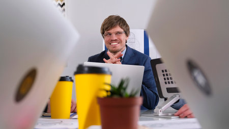Portrait of a happy, smiling businessman. A man in a blue suit is sitting at a table with laptops...