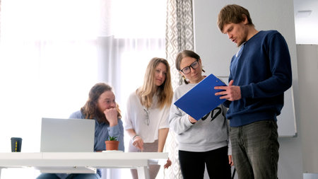 Colleagues are discussing a logo sketch. A group of people is standing around the director's desk with a blue folder in their hands. The scene is collaborative and focusedの写真素材