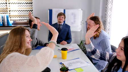 Young and happy women and men of the company high-five each other in the conference room....