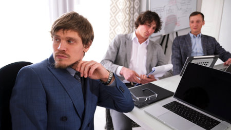 Portrait of a successful representative financier and economist. Three businessmen in suits are sitting at a table with a laptop and papers. The scene is serious and focusedの写真素材