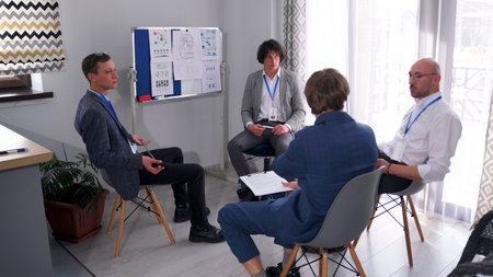 The company's employees are preparing for the meeting. Four male economists are sitting at a...