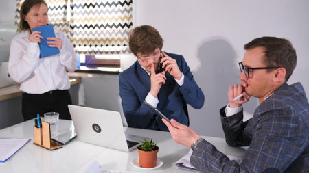 A serious man in a blue suit and glasses is talking on the phone and asks him not to disturb his...