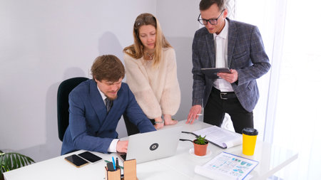 Two colleagues are standing at the director's desk and looking at his laptop screen. Friendly atmosphere in the team. Businessmen are discussing a big project.の写真素材