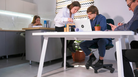 A group of people work together in a cozy family office. A female secretary is sitting at a desk with a laptop. Businesswoman and businessman discuss lawsの写真素材