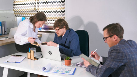 A team of young lawyers is working on a new case. Two men and a woman are sitting at a table in a...