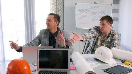 Two male engineers are sitting at a table in a meeting room and are furiously discussing the details...