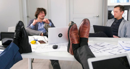 Four men are sitting at a table with their legs up. Architects and designers are working on a new...