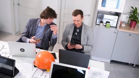 Two design engineers are sitting at a table with laptops in the meeting room and looking at their...