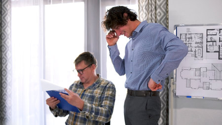 Two men are working together on plans for a construction site. The chief engineer with glasses is...