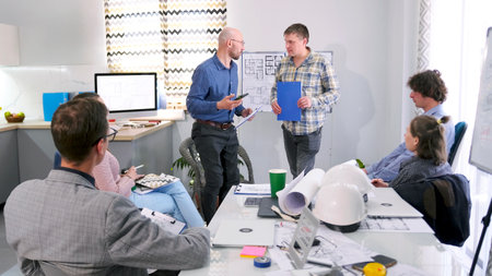 Two male engineers are making a presentation. A group of people is in a conference room discussing a...