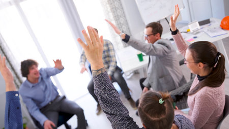 A team building event. A group of people is in a conference room and raising their hands in the air....