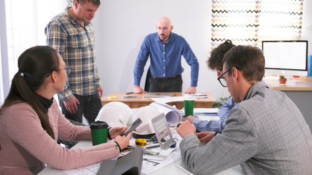 A group of people is sitting at a table in a meeting room and listening to a man standing.