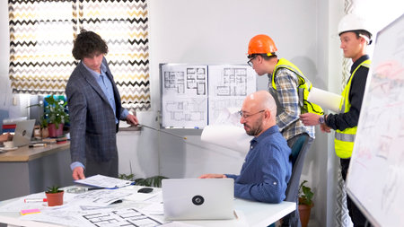 A group of men are discussing plans to build a modern business center. The contractor, foreman, and...