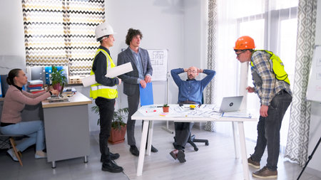 A group of construction workers, an engineer and an architect gathered around a table with drawings....