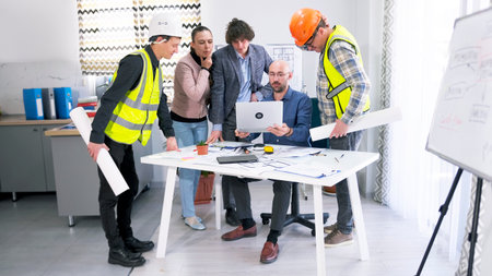 A group of people is looking at the construction drawings of a business building on a laptop screen....