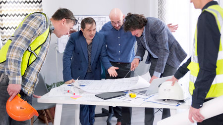 A group of men gathered around a table with blueprints. Discussion of the smart home project....