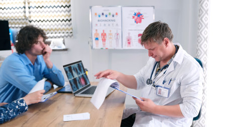 A male therapist looks at the patient's tests. The doctor is sitting at a table with a guy and his...