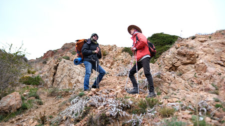 Two travelers are resting halfway up the mountain. The wanderers are standing on a rocky hill and...