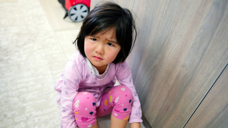 A sad little girl is sitting on the floor in pink pajamas and is about to cry. Children's problems.