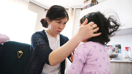 A caring mother looks attentively at her little daughter. A woman helps a young girl in pink pajamas...