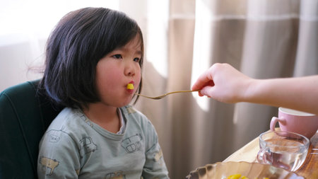 The child does not want to eat. Close-up of a mom feeding her little daughter with a fork. A little girl reluctantly eats lunch. The kid doesn't eat muchの写真素材