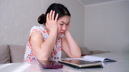 A woman is sitting at a table with a tablet and a mobile phone. She is trying to deal with the work...