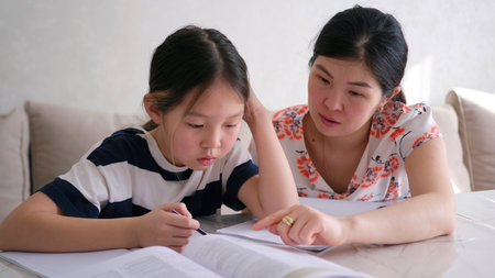 A woman helps a little girl to do her homework at school. Education, training, and parenting. A...