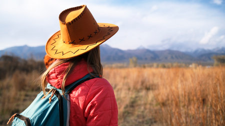 Close-up view from the back of a woman in a cowboy hat looking at the mountains. A traveler went on an autumn hike in the mountains. Trekking, hikingの写真素材