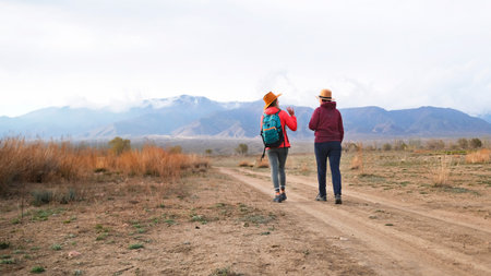 Two female travelers are walking along a dirt road in a wild desert area. Tourists are walking...
