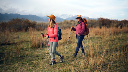 Two tired women are walking through a grassy field after a hard day of hiking. Traveling in the...