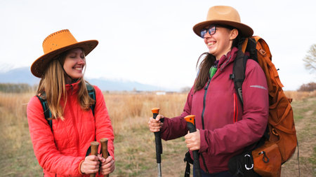 A couple of happy, smiling young female students are standing in a field and joking about their...
