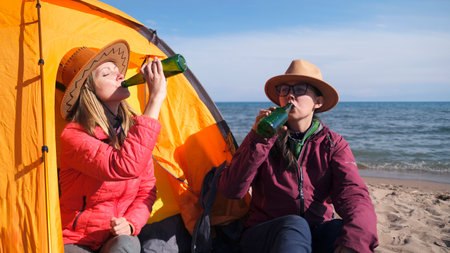 Two tourists drink at a tent on the beach. Two tired travelers are relaxing by the sea. Freedom, relaxation and unity with nature. A date between two loversの写真素材