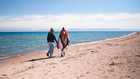 Two women in love holding hands and walking along the beach. Tourists wander along the shore of the blue lake. Freedom and unity with nature. Travel and adventuresの写真素材