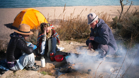 Family vacation in the wilderness by the sea. A man and his adult daughters light a bonfire to cook...