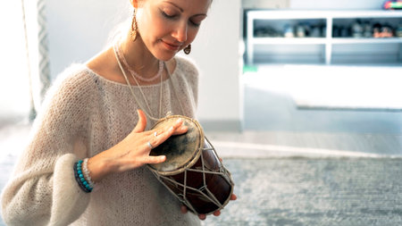 A focused young beautiful student is beating the rhythm on a small drum. The woman smiles and holds a drum in her hands and enjoys her playing and music.の写真素材