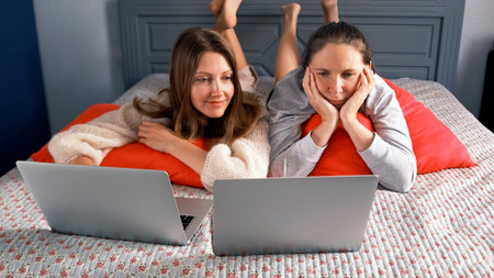 The roommates are lying on the bed and watching movies on their laptop. Two lesbians having fun in the bedroom. The scene is relaxed and laid-backの写真素材