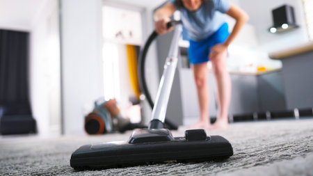 Close-up of the maid vacuuming the carpet in the living room. A woman cleans her house with a vacuum cleaner. The concept of diligence and responsibility, the cleaner worksの写真素材