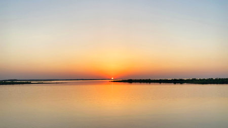 Aydarkul Lake in Uzbekistan at sunset. The sun sets over a calm pond, creating a serene and peaceful atmosphere. The sky is painted in orange and pink tonesの写真素材