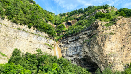 View of a small mountain waterfall along the mountain road from the village of Laza to the village of Kuzun in Azerbaijan. The waterfall flows down from a rocky cliff. The water is clearの写真素材