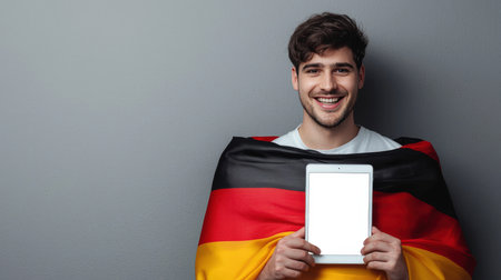 The concept of an invitation to the German presidential election. A mockup of a tablet in the hands of a happy German guy wrapped in the German flag. Tourism and travel in Germany. Immigration and citizenship. Patriotism and pride.の素材