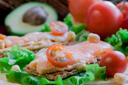 Crispbread with hummus and salmon on vegetable backgroundの写真素材