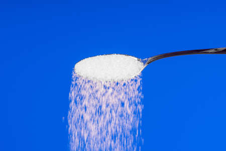 Falling sugar from a spoon on a blue backgroundの写真素材