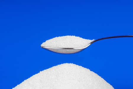 Spoon with white sugar on a blue background