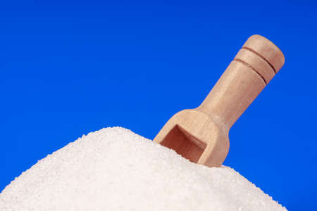 Heap of white sugar with a wooden spoon on a blue backgroundの写真素材