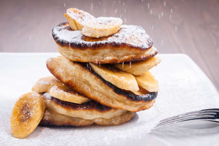 Pancakes with banana and powdered sugar falling on topの写真素材