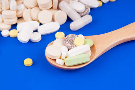 Heap of medical pills with a wooden spoon on a blue backgroundの写真素材