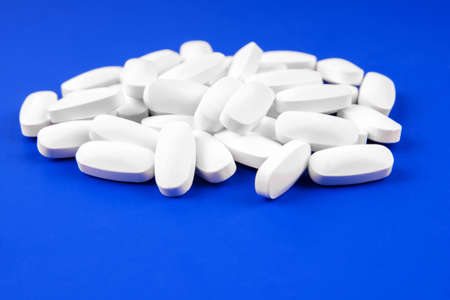 Heap of medical white pills on a blue backgroundの写真素材