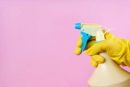 Gloved hand sprays out of a spray bottle on a pink background, copy space, mock upの写真素材